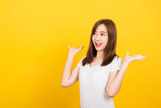 Asian happy portrait beautiful cute young woman teen standing surprised excited screaming open mouth raise hand looking to side away isolated, studio shot on yellow background with copy space