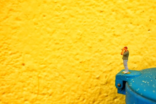 Miniature Figure Photographer with Yellow Painted Concrete Wall Background.