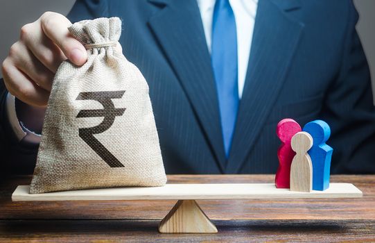 Man puts indian rupeemoney bag on scales with a family. Help aid migrants. Charitable donations, invest in human capital. Social assistance, financial support for who in need, vulnerable populations.