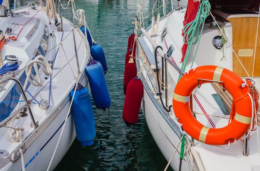 detail of two boats anchored with the typical colored fenders and the characteristic orange life-buoy