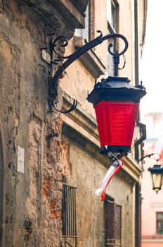 Fragment of an ancient wall with an old street lamp with red cloth and ribbons with national Polish colors in Lublin, Poland