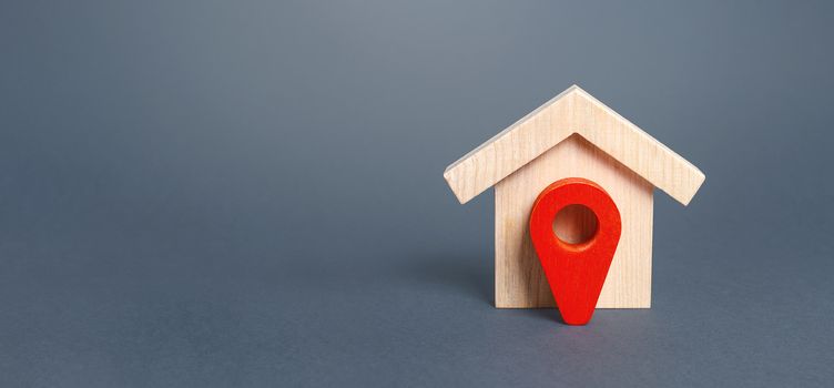 Figurine wooden house and red location pointer. The concept of the location of a building, surrounding infrastructure and the creation of a route to arrive. Moving to another house. Search for options