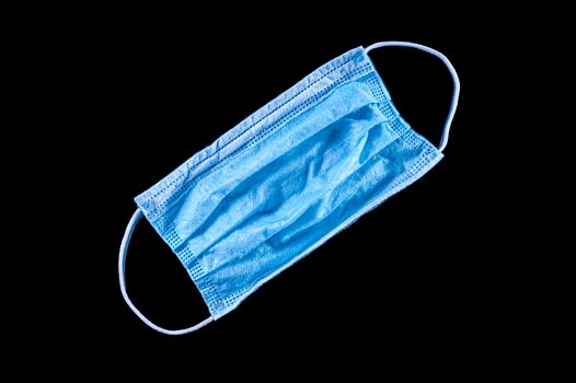 A blue medical surgical face mask on isolated black background