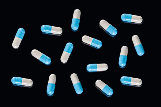 Flat Lay of many blue and white two-piece capsules on an isolated black background. Top view