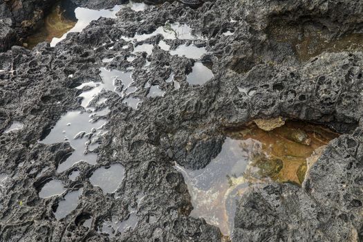 Depressions in a rock with white sand at the bottom, flooded with sea water. Small ponds excavated in lava bed on Indian Ocean coast, Bali, Indonesia. The tide dug out small lakes in the black rock.