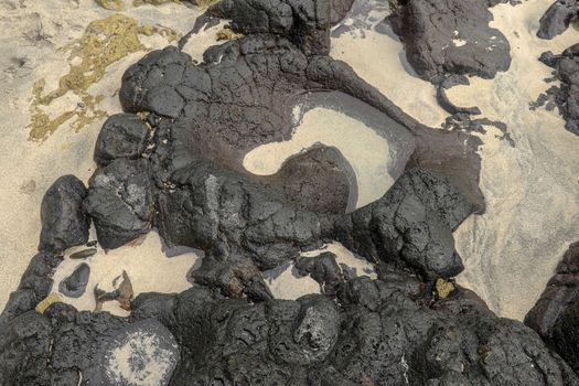 Depressions in a rock with white sand at the bottom, flooded with sea water. Small ponds excavated in lava bed on Indian Ocean coast, Bali, Indonesia. The tide dug out small lakes in the black rock.
