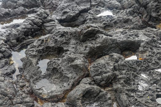 Depressions in a rock with white sand at the bottom, flooded with sea water. Small ponds excavated in lava bed on Indian Ocean coast, Bali, Indonesia. The tide dug out small lakes in the black rock.