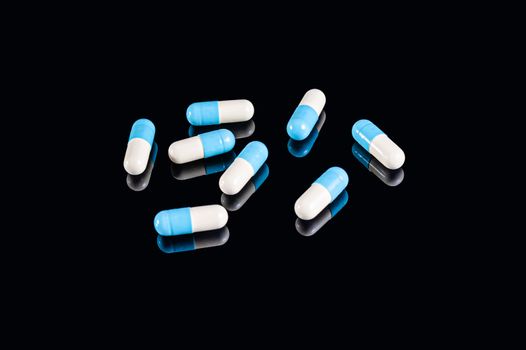 Blue and white two-piece capsules on an isolated black background with reflection
