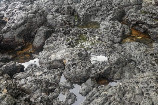 Depressions in a rock with white sand at the bottom, flooded with sea water. Small ponds excavated in lava bed on Indian Ocean coast, Bali, Indonesia. The tide dug out small lakes in the black rock.