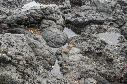 Depressions in a rock with white sand at the bottom, flooded with sea water. Small ponds excavated in lava bed on Indian Ocean coast, Bali, Indonesia. The tide dug out small lakes in the black rock.