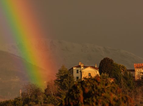 after the rain the colored rays of the sun draw a rainbow on the hill