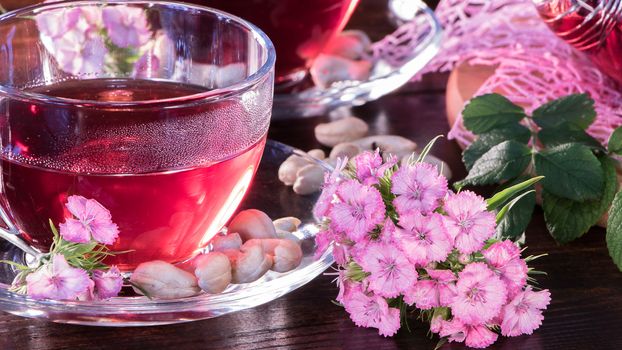 Hibiscus Red tea mug with carnation flowers close-up horizontal photo.English tea tradition.Medicinal therapy based on medicinal herbs and decoctions.Spicy herbs and medicinal broths.A relaxing drink