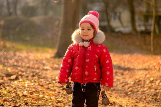 Little girl in red walks in autumn park