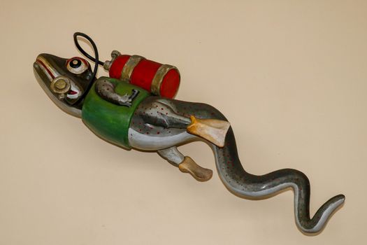 Statue of gecko with diving equipment on the wall of diving center. 3D gecko as a diver. Lizard figurine with green jacket, red diving tank and yellow fins. A funny accessory in the diving base area.