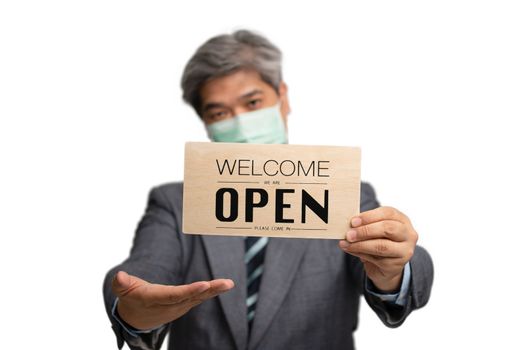 Asian businessman wear medical masks on the isolated background and holding welcome we are open sign. The concept of businesses and shops has to open after the situation began to unwind.