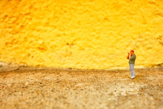 Miniature Figure Photographer with Yellow Painted Concrete Wall Background.