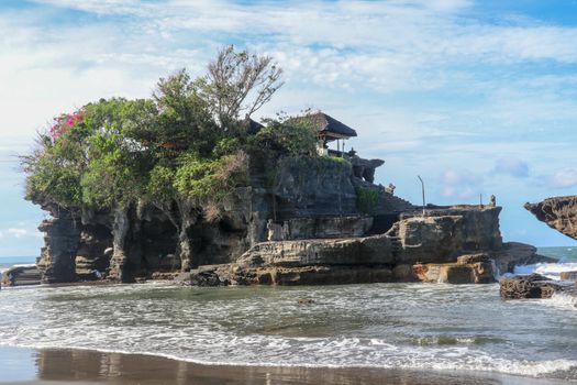 Sacred Balinese temple in Tanah Lot. Pura Batu Bolong on coastline with hole in rock. Traditional style and architecture of Bali. Holy place for local indonesian people