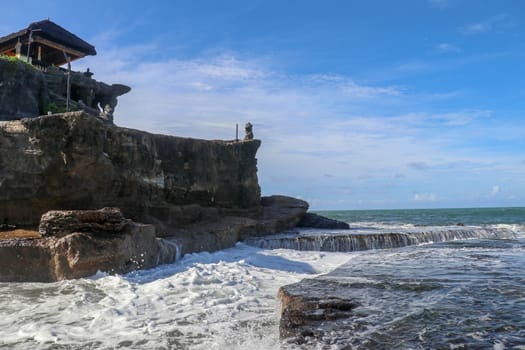 Beautiful balinese landscape. Ancient hinduism temple Tanah lot on the rock against sunset sky. Bali Island, Indonesia. famous Tanah Lot Temple on Sea in Bali Island Indonesia with blue sky and waves.