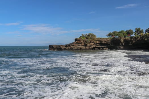 Indian Ocean coast near the Sacred Balinese temple Tanah Lot. Pura Batu Bolong on the edge of a cliff at coastline with hole in the rock. Holy place for local indonesian people