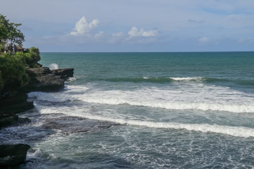Indian Ocean coast near the Sacred Balinese temple Tanah Lot. Pura Batu Bolong on the edge of a cliff at coastline with hole in the rock. Holy place for local indonesian people