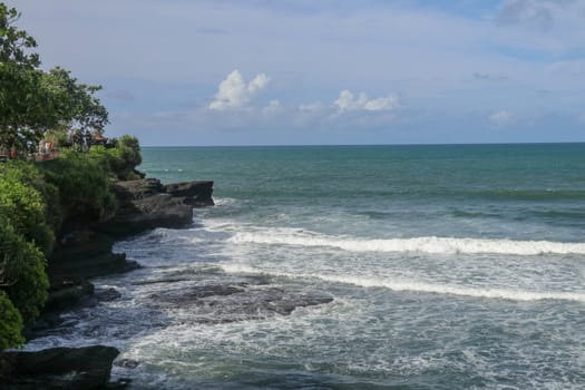 Indian Ocean coast near the Sacred Balinese temple Tanah Lot. Pura Batu Bolong on the edge of a cliff at coastline with hole in the rock. Holy place for local indonesian people