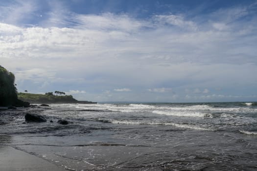 Indian Ocean coast near the Sacred Balinese temple Tanah Lot. Pura Batu Bolong on the edge of a cliff at coastline with hole in the rock. Holy place for local indonesian people