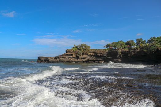 Indian Ocean coast near the Sacred Balinese temple Tanah Lot. Pura Batu Bolong on the edge of a cliff at coastline with hole in the rock. Holy place for local indonesian people
