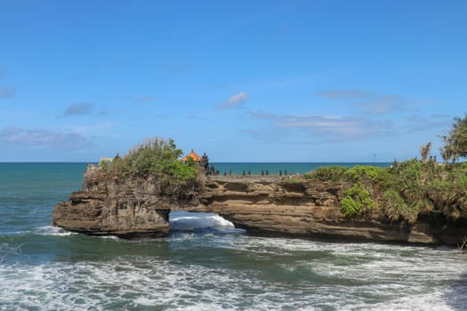 Indian Ocean coast near the Sacred Balinese temple Tanah Lot. Pura Batu Bolong on the edge of a cliff at coastline with hole in the rock. Holy place for local indonesian people