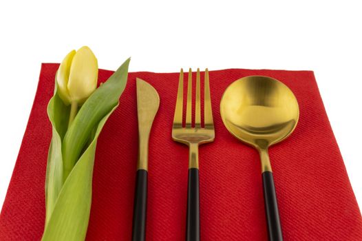 Gold cutlery and yellow tulip neatly displayed on a red place mat symbolic of a spring table setting and the season