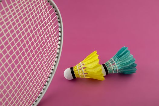 Badminton rackets and colorful feathered shuttlecocks in green and yellow on a pink background