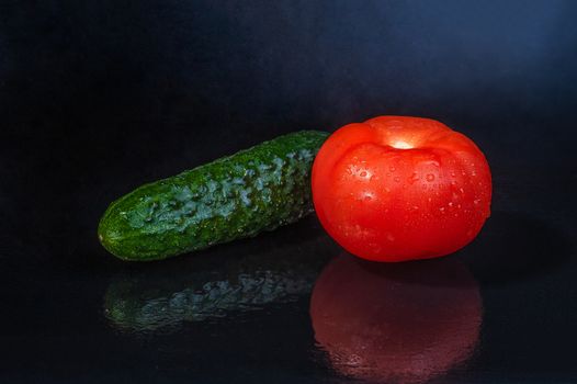 fresh vegetables - green cucumber and red tomato on an isolated black background with reflection