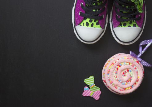 Top view of violet sneakers and lollipop on black board, with copy space