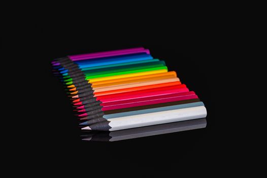 many colored pencils of different colors on an isolated black background with reflection