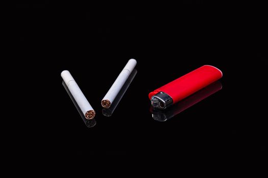two white filter cigarettes and a plastic gas red lighter on an isolated black background with reflection