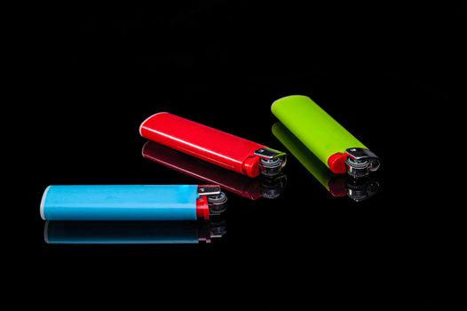 blue, green and red plastic gas lighters on an isolated black background with reflection