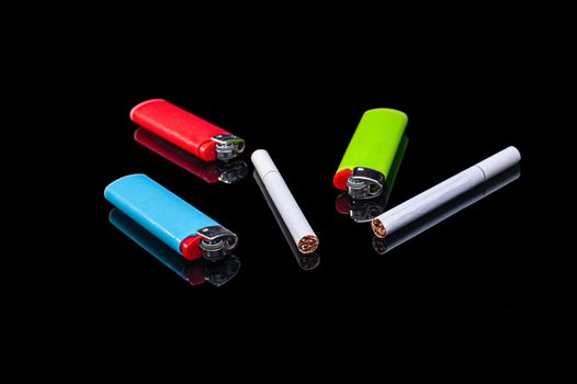 white filter cigarettes and plastic gas lighters of different colors on an isolated black background with reflection