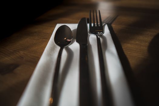 Some silverware, cutlery sat on a white napkin on a wooden table in a cafe setting