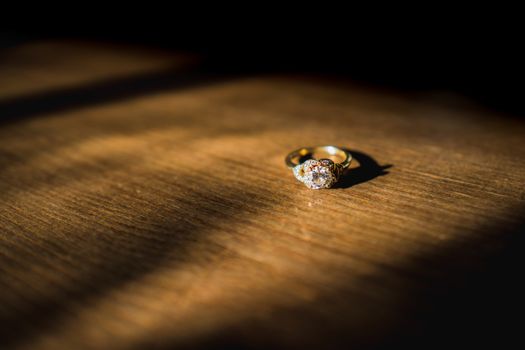 A gold diamond engagement ring sat on a wooden table in natural daylight