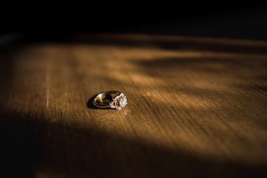 A gold diamond engagement ring sat on a wooden table in natural daylight