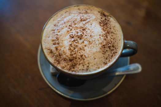 A cup of cappuccino coffee on a wooden table in a cafe setting