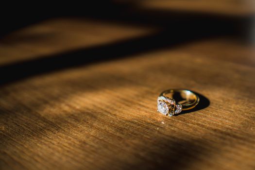 A gold diamond engagement ring sat on a wooden table in natural daylight