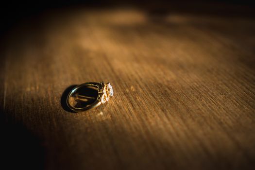 A gold diamond engagement ring sat on a wooden table in natural daylight