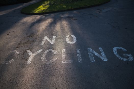 A painted No Cycling sign on the pavement at the entrance of a local park in the UK