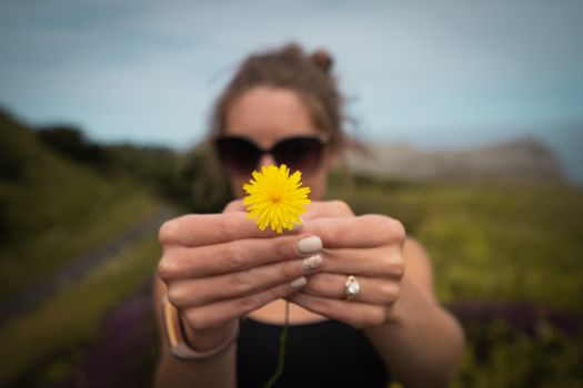 A portrait of a woman holding a yellow dandelion flower close up