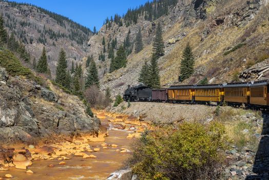 Historic steam engine train travels from Durango to Silverton through the San Juan Mountains along the Animas River in Colorado, USA.