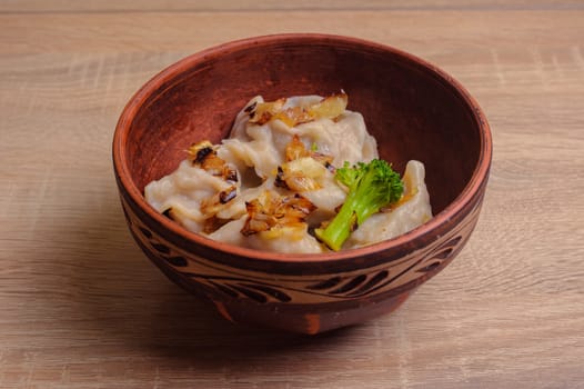 dumplings (pierogi, varenyky) with fried onions and broccoli in a brown clay plate with ornament