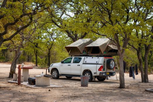 Halali, Namibia - March 27, 2019 : Tent located on the roof of a pickup 4x4 car parked under trees of Halali camp in Etosha National Park.