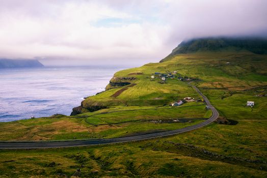 Road going to Gasadalur village surrounded by beautiful faroese landscape and Atlantic Ocean on the island of Vagar, Faroe Islands, Denmark.