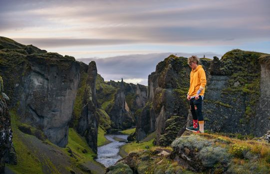 Young hiker standing at the edge of the Fjadrargljufur Canyon in Iceland. Fjadrargljufur Canyon is about 100 meters deep and about 2 kilometers long and it is located in South East of Iceland.