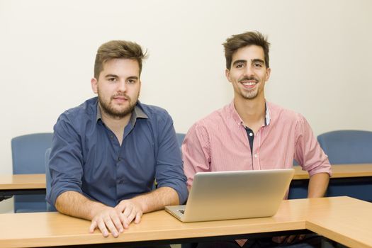 two young happy men at the classroom with a computer